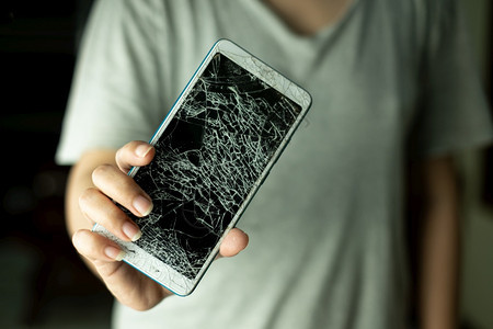 制动丁香断裂的女人站着拿智能手机的屏幕黑背景被打碎了图片
