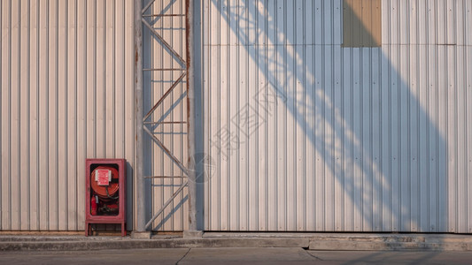 古老的红色应急柜子和在水泥地板上有阳光和影子的铁板墙壁表面水泥地板上锈制金属高地路标牌结构工厂建筑的金属板墙壁表面有阳光和阴影工图片