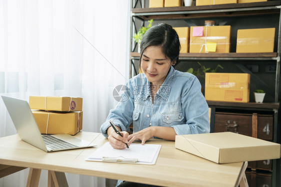 在线的女士卖方近手亲拉年轻亚洲妇女打手提笔记本电脑键盘检查在线订单货物库存交付包运送邮寄的亚洲妇女在家庭办公室开小企业查看图片