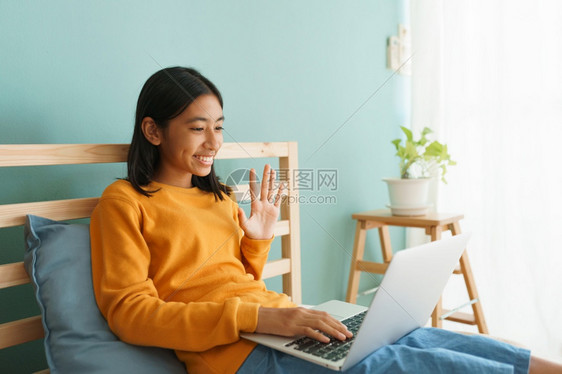 称呼快乐的亚洲女孩在家中庭内部笔记本电脑上用打贺礼在线辅导员时挥手距离初级图片