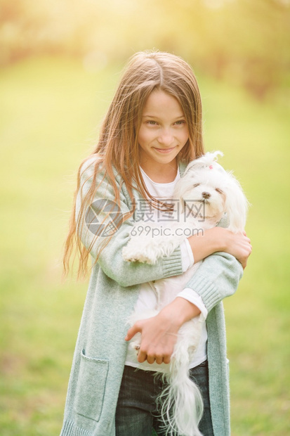 娱乐宠物幸福快的小女孩在大自然中养着一只狗女孩在公园里和一只马耳他小狗玩耍微笑的小女孩在公园里玩耍和拥抱小狗图片
