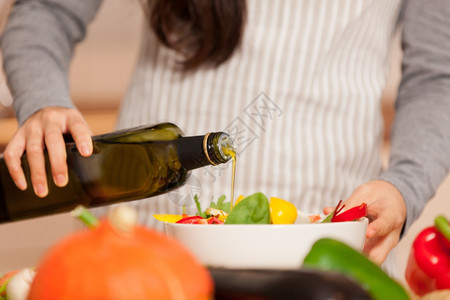 美味的女液体把橄榄油倒入多彩色沙拉的女人紧地关上图片