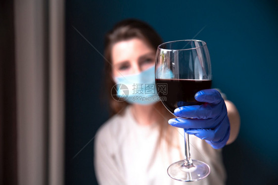 妇女在家里戴保护面罩和蓝手套在家中喝红酒为CoronaCovid19自我隔离在家中戴保护面罩和蓝手套喝红葡萄酒的悲伤和孤单近身女图片