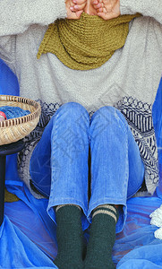 工艺妇女穿着蓝色牛仔裤白羊毛衫袜子和苔绿色羊毛围巾与蓝背景坐在一起编织手工制作产品为业余爱好冬季取暖越南手工制作的图片