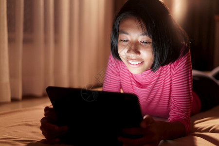 在线的笔记本电脑自己快乐的亚洲女孩透过互联网在平板电脑上学习晚在卧室亚洲孩童观看和电脑教育距离在家微笑学习概念NationsLe图片
