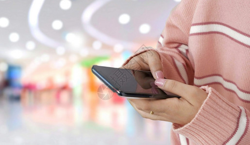 无线的移动反射使用智能手机在购物场所生活方式和技术概念背景模糊的下用智能手机亲近粉红色毛衣的年轻女手图片