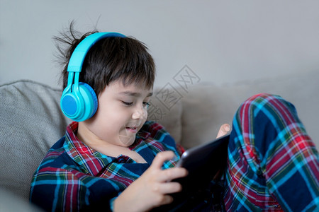 坐着在线的戴耳机听音乐的快男孩带着笑脸的子在度假时与朋友平板电脑上玩线游戏穿着圣诞睡衣的孩子早上在家放松白色的图片
