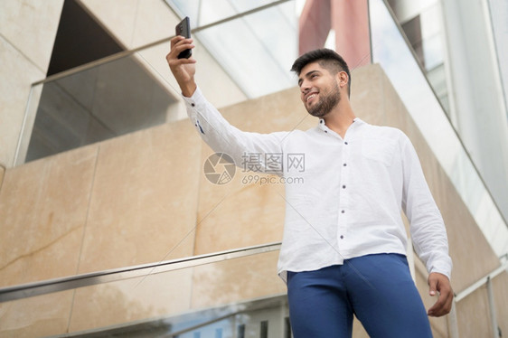 技术成人自己年轻英俊的西班牙裔男子在户外用智能手机自拍高质量照片年轻英俊的西班牙裔男子在户外用智能手机自拍图片