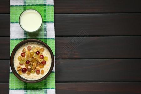 早餐乳制品含葡萄和核桃的燕麦粥在生锈碗中加葡萄和胡桃上面一杯牛奶用自然光照黑木头图片