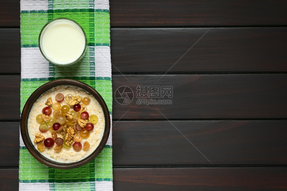 早餐乳制品含葡萄和核桃的燕麦粥在生锈碗中加葡萄和胡桃上面一杯牛奶用自然光照黑木头图片