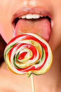 糖果一位年轻美丽的女孩舔着一个多彩明亮的洛利波普Lollipopop她以粉红孤立的背景用她舌头近拍摄照诱惑图片