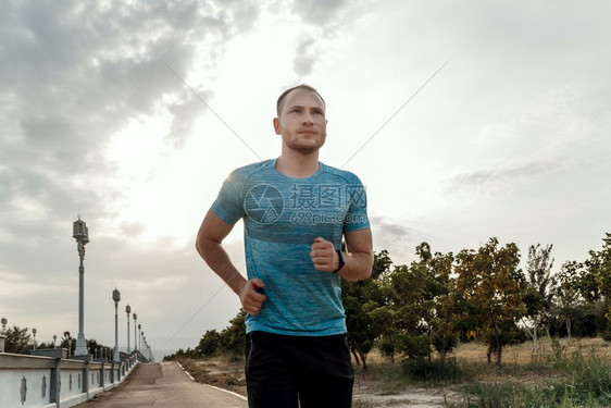 移动慢跑穿着蓝色T恤和黑短裤的白人男子肖像他们在日落时沥青轨道上培训和运行活力图片
