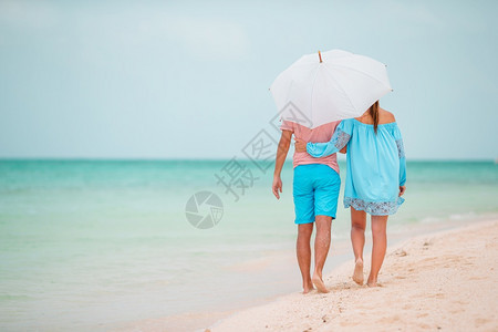 年轻情侣撑伞在沙滩上散步图片