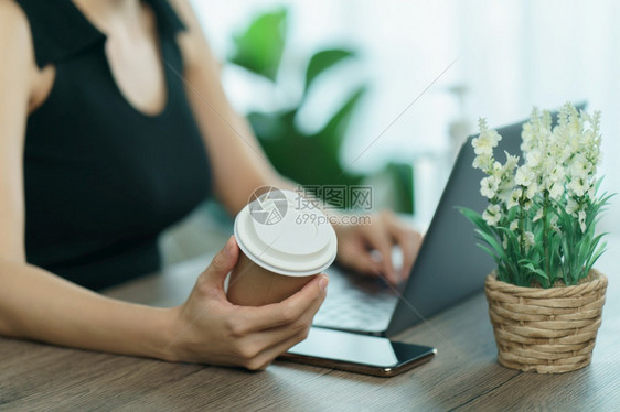 一次年轻妇女用一次咖啡杯喝并在工作桌上使用电脑笔记本工作场所女图片