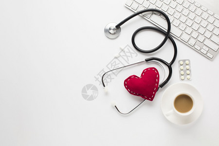 桌子便携的清爽红色心脏听诊器靠近药品咖啡键盘白桌图片