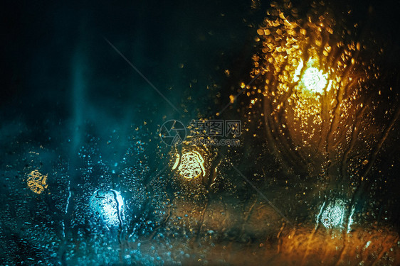驾驶粗糙的丰富多彩黄昏和bokeh灯光下车边玻璃上的水滴图片