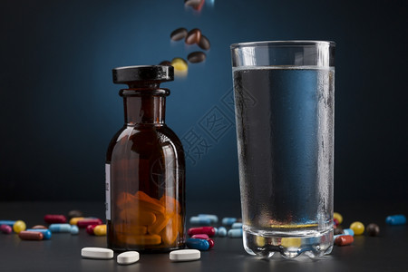 疾病医疗的五颜六色药瓶丸和一杯饮料水药瓶丸和一杯冷饮水药剂图片