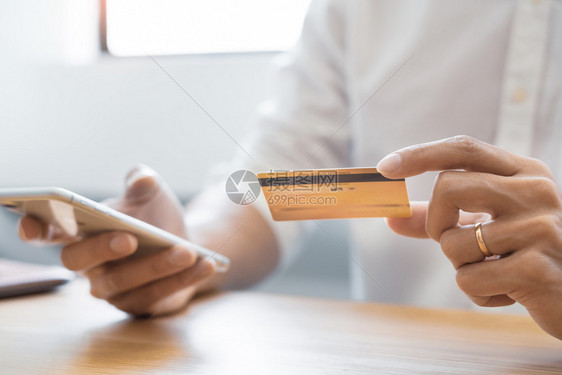 聪明的坐着人们手持临时衬衫的男子用信卡支付工资使用智能电话利移动银行应程序在线付款通过互联网在上购物下订单Onlinepay图片