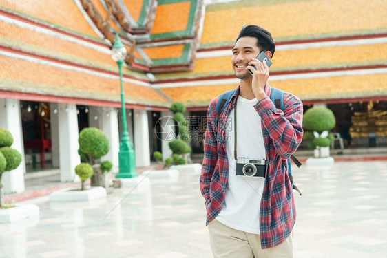 亚洲男游客在夏季时泰国曼谷的WatSuthatThepwararamRatchaworawihan步行谈论智能手机和微笑独自旅行图片