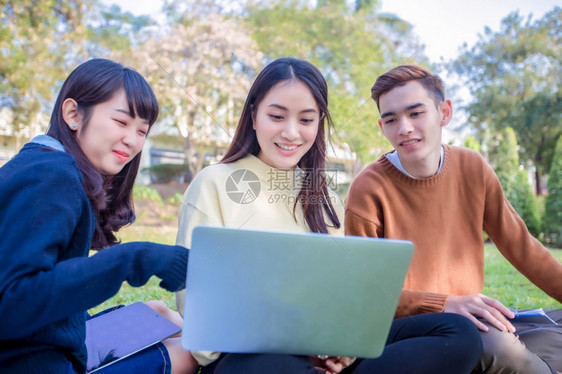 大学生们一起微笑着坐在草地上工作图片