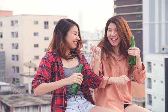 庆典喝鸡尾酒两个亚裔妇女饮酒在屋顶派对户外庆祝友谊女男双和变者夫妇图片