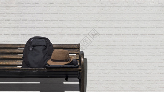 泰国在公共园区白色砖墙背景前的金属公园长椅上装有手提笔记本和黑色背包的联邦老旧帽子黑色的假期图片
