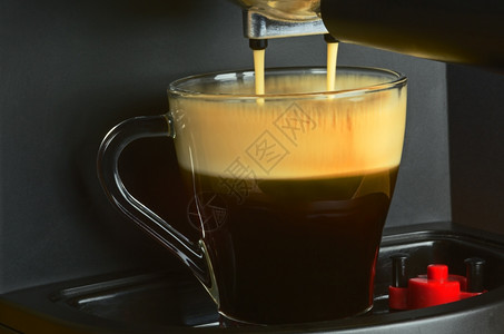 制造传统的对咖啡机在有趣的大气光线下倾注浓缩的咖啡以清晰可见略微不明显尖锐的蒸气向咖啡及其表面水平视图A上喷洒泡沫的浓咖啡机进行图片