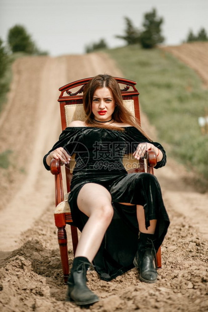 身着黑裙子的漂亮年轻美女为一位坐在沙路上经典扶手椅的摄影师做姿势女淑景观图片