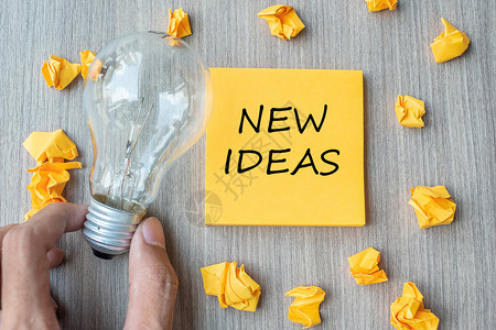 成就以黄色注字写的新思想文和破碎的纸商家用灯泡在木桌背景上架着灯泡创意新想象灵感解决方案战略和目标概念明亮的成功图片