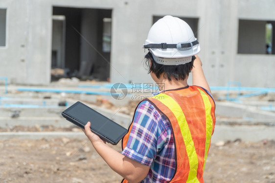 药片漂亮的在建筑工地上站着时用平板头戴盔的亚洲女建筑工肖像以背景概念为构筑工程想吸引人的图片