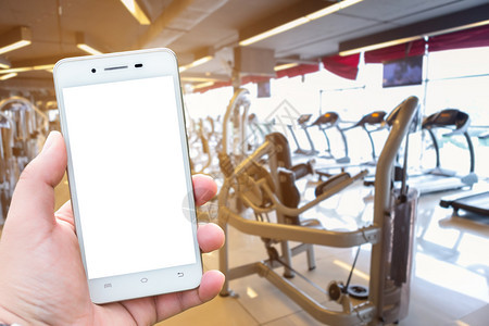 屏幕手持智能机模糊图像的AwHand持有智能手机模糊图像触摸体育健身室内俱乐部和康俱乐部的重点不集中体育锻炼设备为Gym模糊背景图片