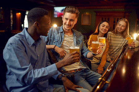 夜店生活晚四个朋友在酒吧的柜台喝啤一群人在吧放松夜间生活方式友谊动庆祝四个朋友在酒吧的柜台喝啤图片