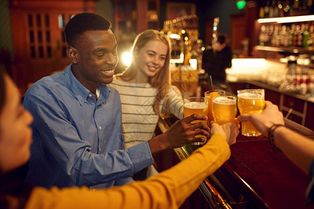 晚上室内的四个快乐朋友在酒吧柜台喝啤一群人在吧放松夜间生活方式友谊四个快乐的朋友在酒吧喝啤图片
