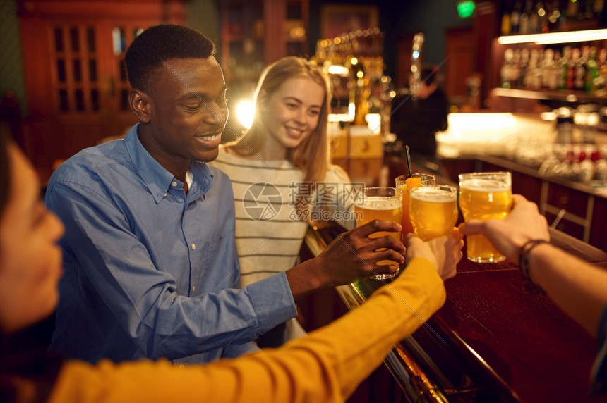 晚上室内的四个快乐朋友在酒吧柜台喝啤一群人在吧放松夜间生活方式友谊四个快乐的朋友在酒吧喝啤图片