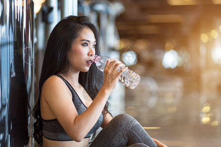 美丽亚洲人坐着参加体操室内健身俱乐部和的亚洲妇女用一瓶水喝运动会图片