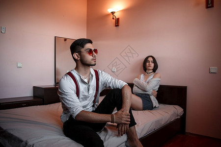 相互作用不开心年轻的一个戴眼镜年轻时尚男子和一个坐在床上的年轻女孩一个离女孩更近的男人有选择地关注她图片