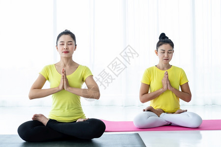 身体合黄色的两名亚洲年轻妇女在健身房练习瑜伽穿黄色礼服或与训练员和实习者一起表演冥想健康生活方式和健康概念图片
