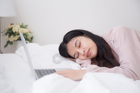 无聊亚洲妇女睡觉是因为她们厌倦了在卧室用笔记本电脑工作概念生活方式和在家工作所以她们在睡觉互联网夜晚图片