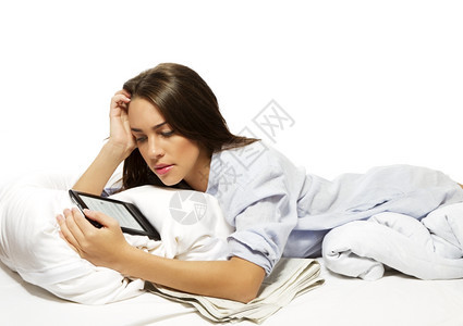 美丽的女人在床上阅读电子书美丽的女人在床上阅读白色背景的电子书个人脑移动图片