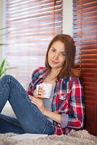 微笑年轻的热漂亮姑娘在家沙发上喝咖啡茶图片