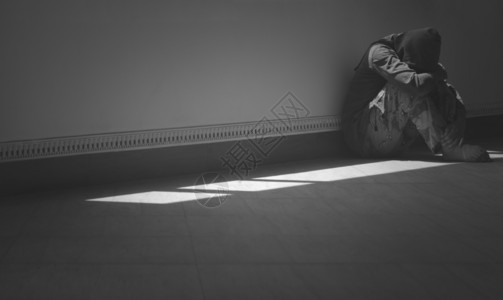心灰无望男人的侧面景色独自坐着拥抱他的膝盖在房间角落的地板上黑暗