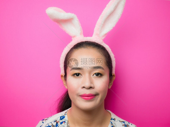 乐趣脸穿着兔子耳朵头带和粉红背景的可爱少女复活节时穿兔子耳朵头带的妇女在有吸引力的年轻女青中戴着兔子耳朵头带微笑着明亮的粉红背景图片