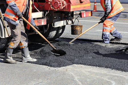 团体公路工人quuu作组将部分路面的沥青换成新鲜并修整在道路建设中修理工作组在道路建设中用铲子重新修筑部分沥青构造建图片