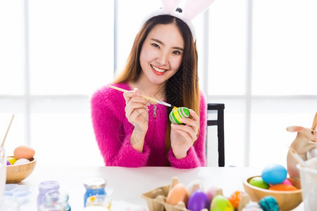 染色象征复活节的概念带着兔子耳朵的亚洲快乐年轻女披着兔子耳朵的青春少女为复活节画了鸡蛋在白衣室背景下颜色图片