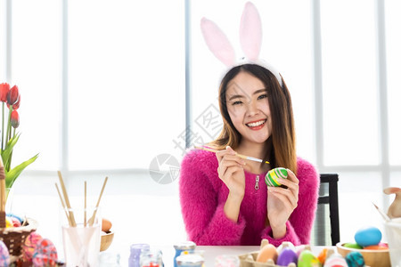 象征可爱的复活节概念带着兔子耳朵的亚洲快乐年轻女披着兔子耳朵的青春少女为复活节画了鸡蛋在白衣室背景下有色图片