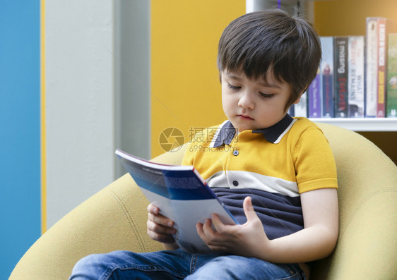 学校教育步的儿童孤独地坐在书店里孤单地坐在书上看着的无趣小男孩肖像独自在图书馆看时脸都无聊的孔面沉闷深悲伤和忧的难受小男孩图片