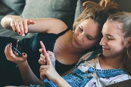 年轻妇女使用移动电话观看音乐短片发信用智能手机向青少年发送信息坐在沙发上家里坐使用技术设备观察音乐剪辑利用智能手机向青少年传递信图片