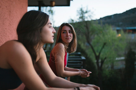 蓝色的两个年轻天主教女青年在阳台上观看日落的光芒树木时尚图片