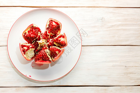 维生素营养成熟和红石榴果实在木制白色背景上的瓷盘分成几块在木制白色背景上的瓷盘成熟的石榴子图片