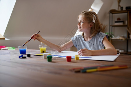 oopicapi坐在桌边的小女孩画着刷子和油漆在艺术学校上讲课的小孩年轻画家愉快的爱好乐童年带着刷子和油漆画的小女孩调色板工艺图片